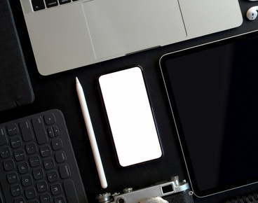 Top view of dark trendy workspace with blank screen smartphone and other electronics with office supplies on dark table background