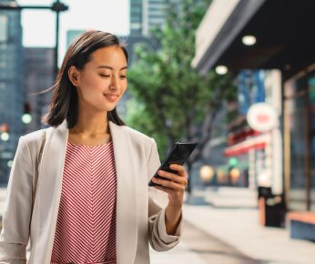 Portrait of an Attractive Japanese Female Wearing Smart Casual Clothes and Using Smartphone on the Urban Street. Manager in Big City Connecting with People Online, Messaging and Browsing Internet.