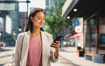 Portrait of an Attractive Japanese Female Wearing Smart Casual Clothes and Using Smartphone on the Urban Street. Manager in Big City Connecting with People Online, Messaging and Browsing Internet.