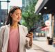 Portrait of an Attractive Japanese Female Wearing Smart Casual Clothes and Using Smartphone on the Urban Street. Manager in Big City Connecting with People Online, Messaging and Browsing Internet.